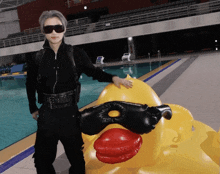 a man in a black suit stands next to a yellow duck float