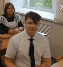 a man in a white shirt and black tie is sitting at a desk