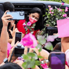 a woman wearing a face mask is holding a bouquet of pink roses while being photographed by a crowd .