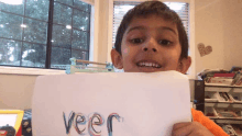 a young boy is holding a piece of paper with the word veer written on it