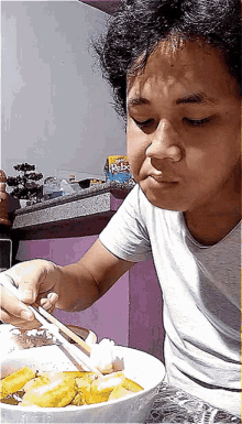 a man is eating a bowl of food with chopsticks and a bottle of kellogg 's on the counter behind him