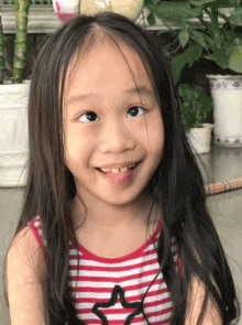 a little girl sticking her tongue out and wearing a red and white striped shirt with a star on it