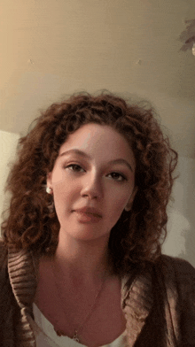 a woman with curly hair is wearing a necklace and earrings