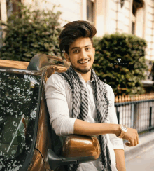 a young man leaning on the side of a car with a watch on his arm