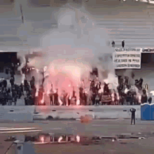 a group of people are standing in front of a stadium with flames and smoke coming out of it .