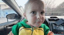 a little girl is sitting in the driver 's seat of a car with a handicapped parking sign in the background