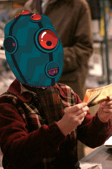 a man wearing a blue robot mask holds a piece of paper in his hand