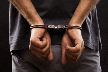 a man in handcuffs has his hands behind his back against a black background