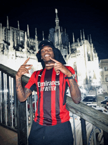 a man wearing an emirates fly better shirt stands on a railing