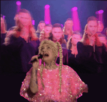 a woman in a pink dress singing into a microphone in front of a crowd