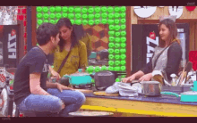 a man and a woman are sitting at a table in a kitchen with pots and pans on it .