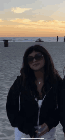 a woman wearing sunglasses is standing on a beach at sunset