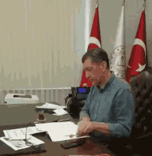 a man sits at a desk in front of three flags including one that says ' turkey ' on it