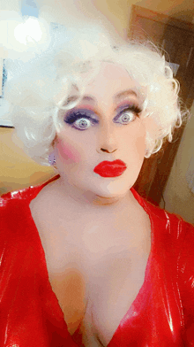 a drag queen with white hair and red lips is wearing a red dress