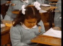 a girl with a bow in her hair sits at a desk in a classroom with latin soapy fever written on the bottom