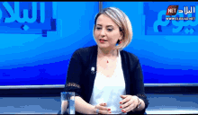 a woman sits at a table with a glass of water in front of a screen that says net on it