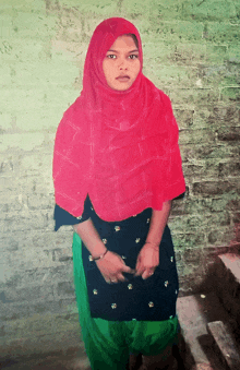 a woman wearing a red head scarf stands in front of a green brick wall