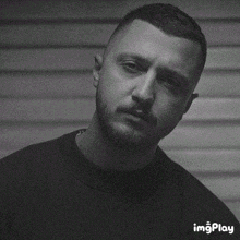 a black and white photo of a man with a beard wearing a black shirt .