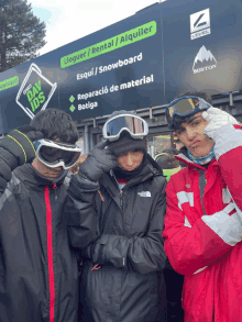 three young men wearing goggles in front of a sign that says burton