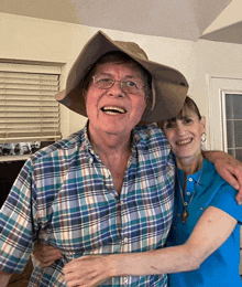 a man wearing a plaid shirt and a hat is hugging a woman