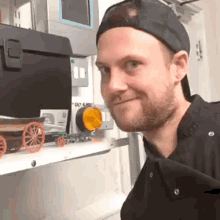 a man wearing a baseball cap and a black shirt is standing in front of a shelf with a toy truck on it .