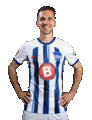 a man in a blue and white striped soccer jersey is standing with his hands on his hips and smiling .