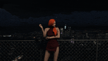 a woman in a red dress is standing on a balcony overlooking a city