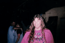 a woman wearing a pink shirt that says sandy smiles for the camera