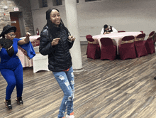 two women are dancing in a room with tables and chairs and an exit sign in the background