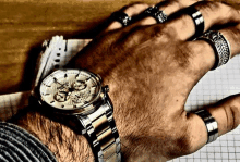 a man is wearing a watch on his wrist and has rings on his fingers