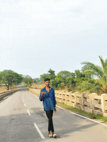 a young man in a blue plaid shirt stands on the side of the road