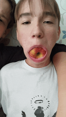 a boy with an apple in his mouth wearing a white shirt with a picture of an angel on it