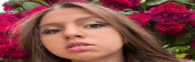 a close up of a woman 's face in front of a bush of red roses .