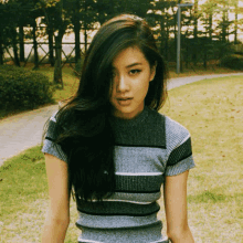 a woman wearing a striped sweater stands in a park