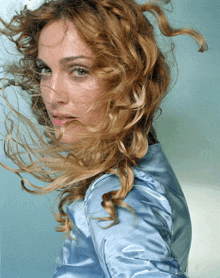 a woman with her hair blowing in the wind is wearing a blue shirt