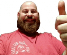 a bald man with a beard is wearing a red shirt and giving a thumbs up .