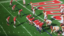 a group of football players are lined up on a field with a large r on the side of the field .