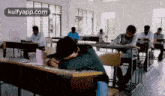 a group of students are sitting at desks in a classroom . one of the students is sleeping on his desk .