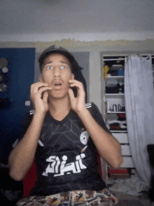 a young man wearing a black shirt with arabic writing on it is making a surprised face