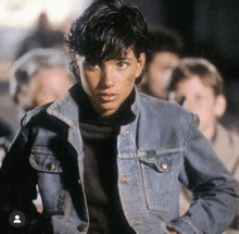 a young man wearing a denim jacket stands in front of a crowd of people