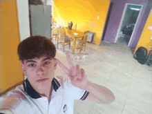 a young man giving a peace sign in front of a yellow wall