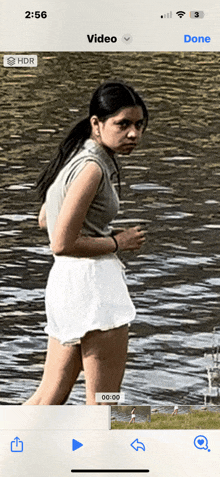 a woman in white shorts is standing in front of a body of water with the time of 2:56