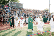 a group of graduates are walking on a field in front of a stadium that says norman schultz field house