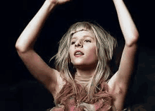 a woman with blonde hair is dancing with her arms in the air in a dark room .