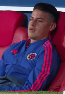 a man in a blue adidas jacket sits on a red chair