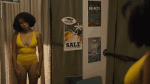 a woman in a yellow swimsuit is standing in front of a wall with posters on it that say sale and surf