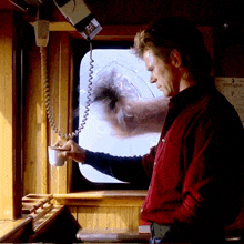 a man in a red shirt holds a cup of coffee in front of a window