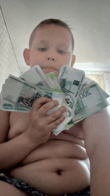 a shirtless boy is holding a stack of russian money in his hands