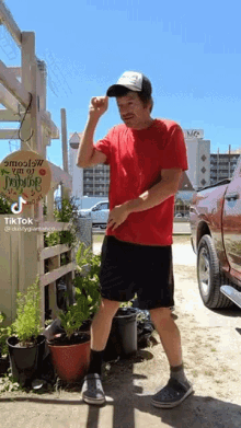 a man wearing a red shirt and black shorts stands in front of a sign that says welcome to the garden