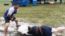 a man in a blue shirt is standing next to a woman in a muddy field with a red cooler in the background